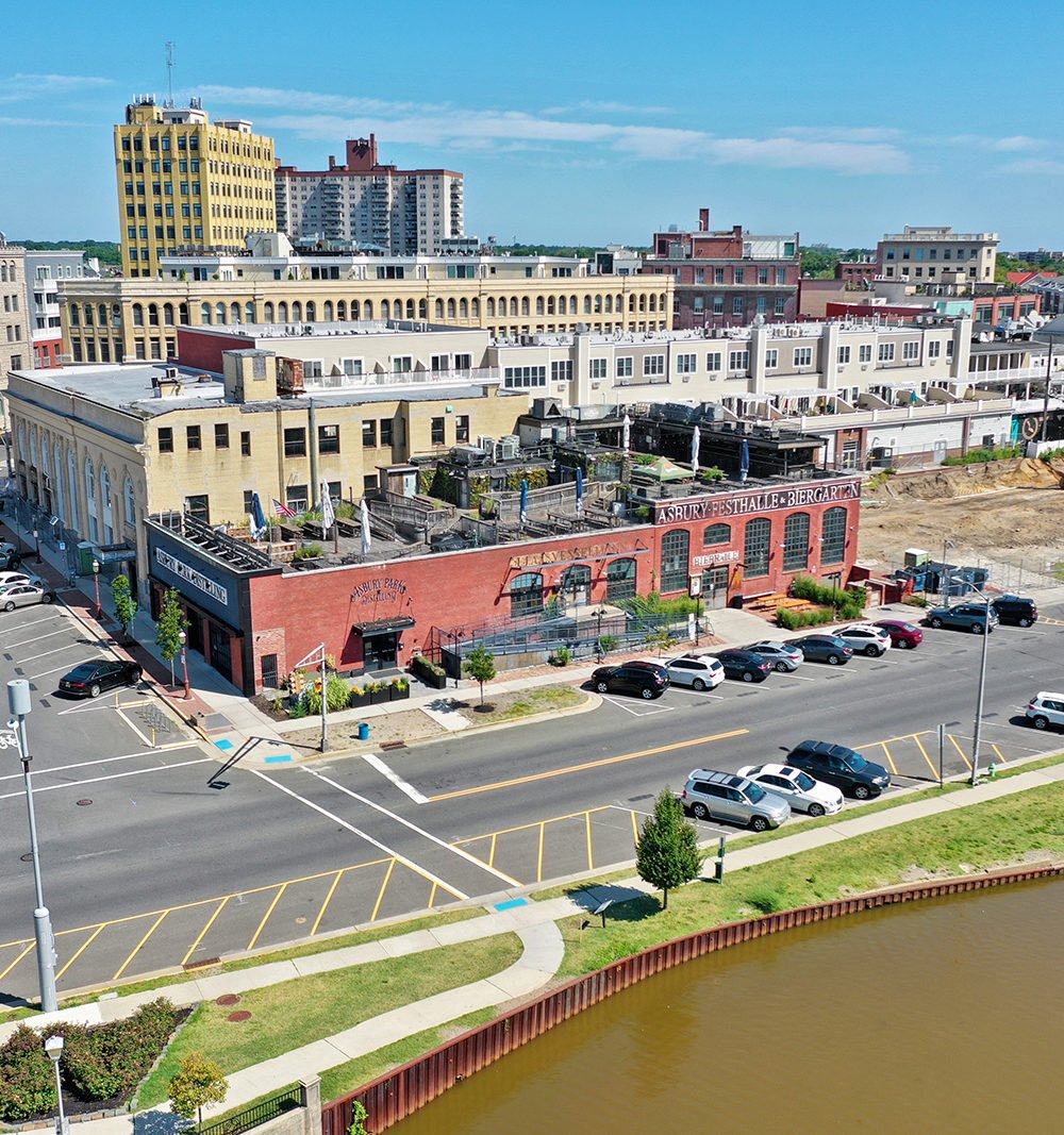 Aerial view of a downtown development beside a canal, with a red-brick biergarten in the foreground.