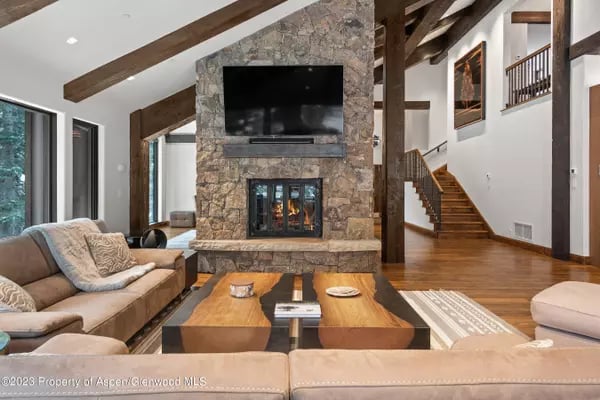 Living room with a stone fireplace, exposed timber beams, and a staircase.
