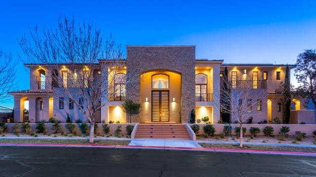 Two-story modern home with a stone-clad entrance and illuminated windows at dusk.