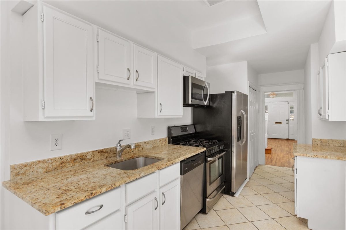 Galley kitchen with white cabinets, granite counters, and stainless steel appliances.