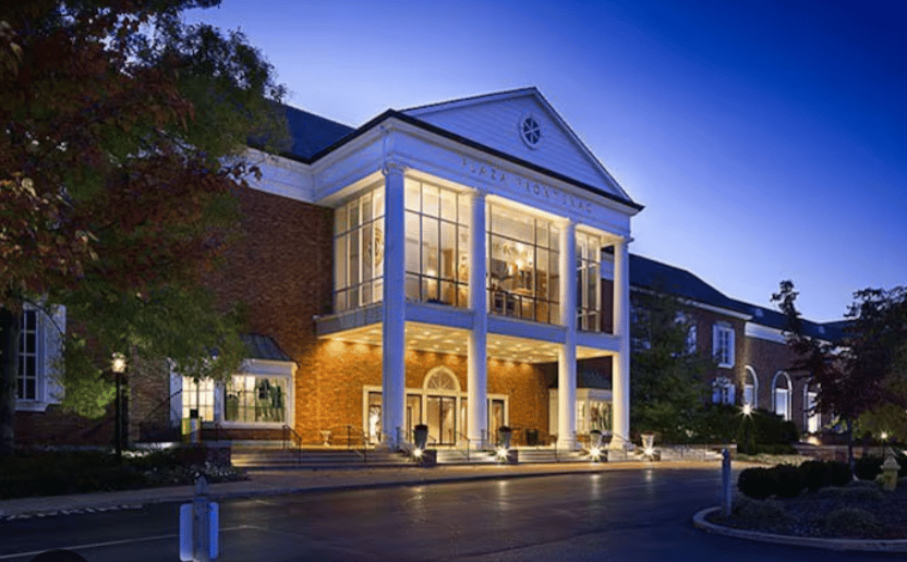 Red-brick building with a columned entrance and glowing windows at dusk.