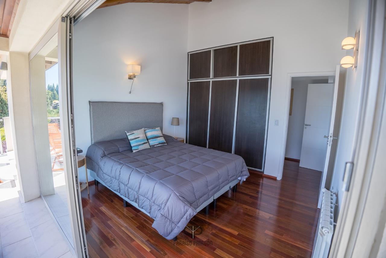 Bedroom with gray quilted bed, dark wardrobes, and open balcony doors.