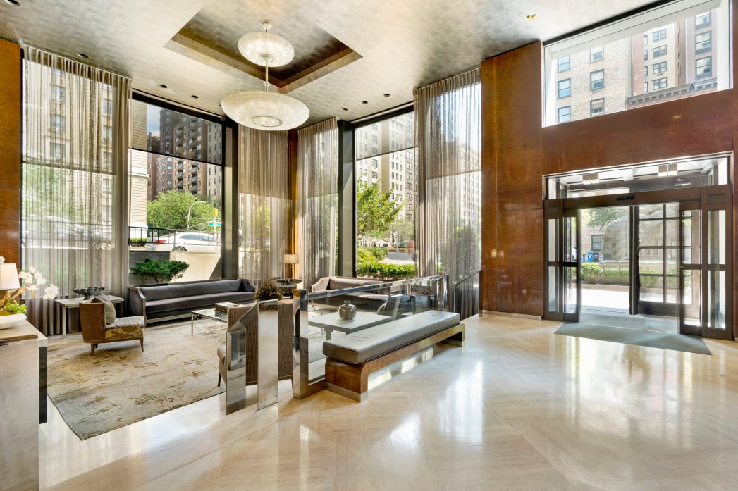 Residential lobby with floor-to-ceiling windows, lounge seating, and a glass entrance.
