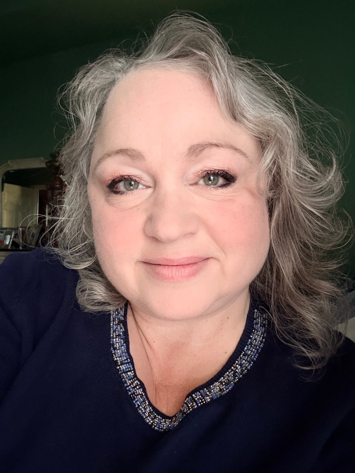 Mathea Ford with wavy gray hair, wearing a dark top with a beaded neckline.