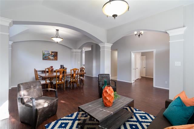 Living and dining area with arched openings, dark wood floors, and a geometric rug.
