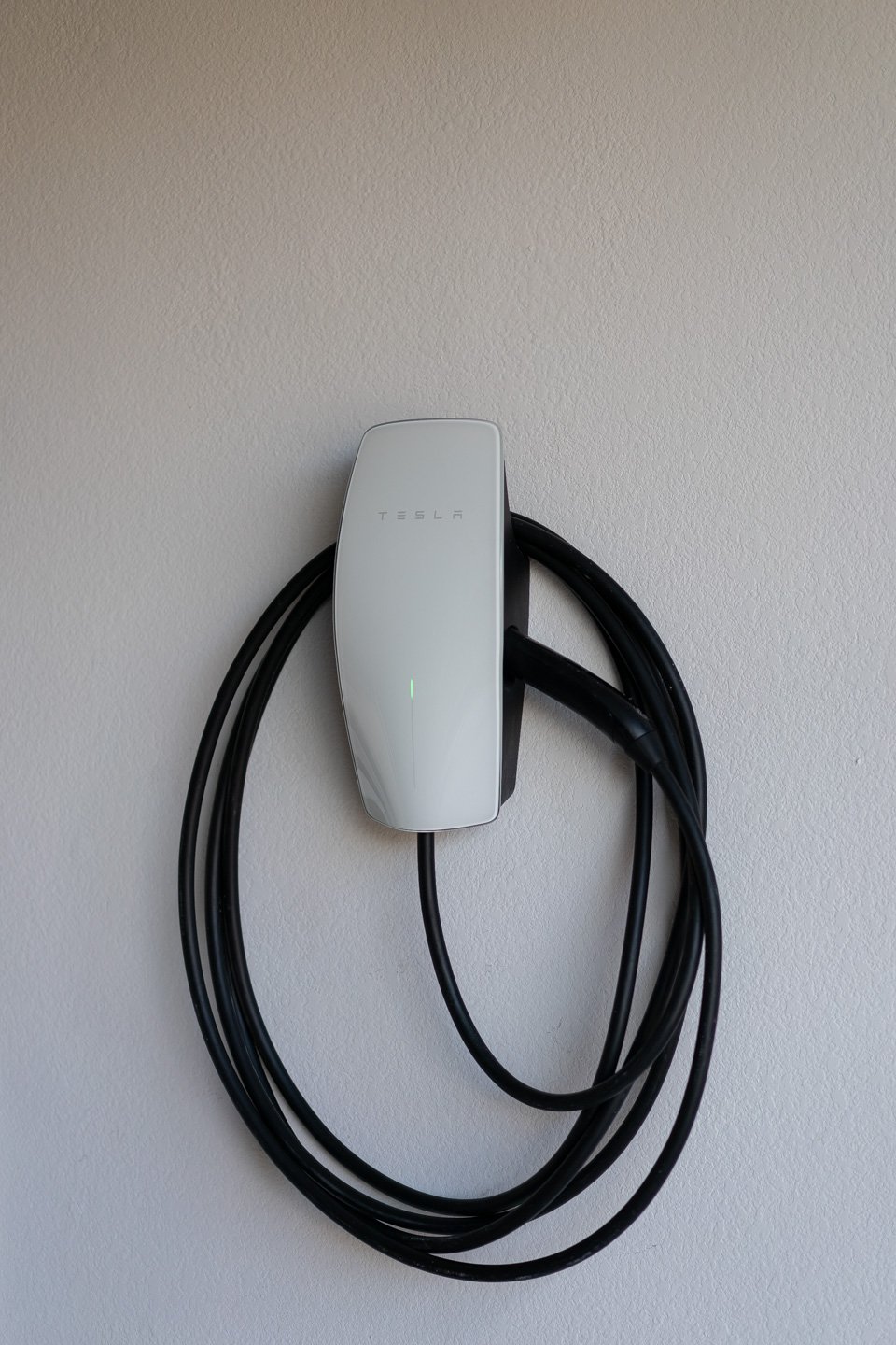 Tesla wall-mounted electric vehicle charger with a long, coiled black cable.