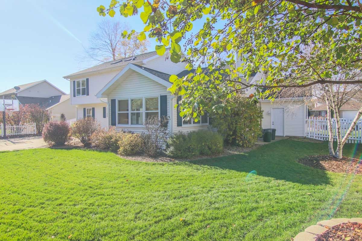 White colonial-style home viewed from a green backyard beneath autumn trees.