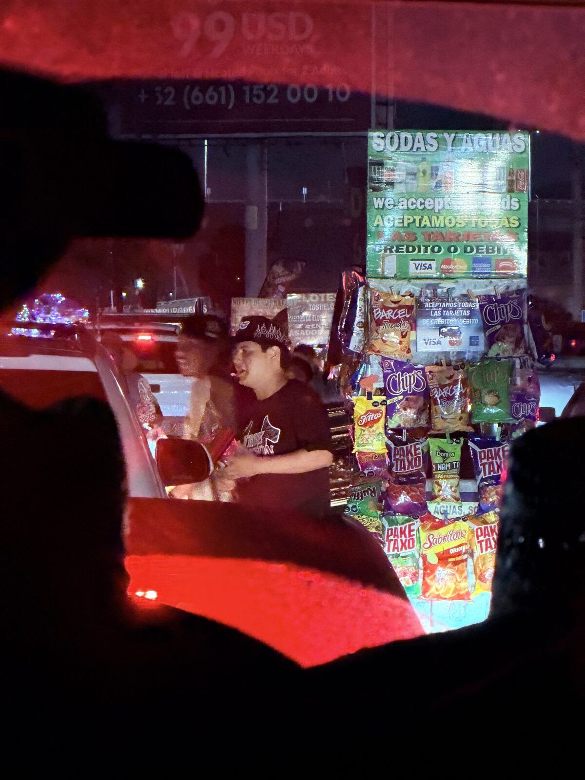 View from inside a car at the border crossing at night, with a vendor selling snacks between lanes of traffic