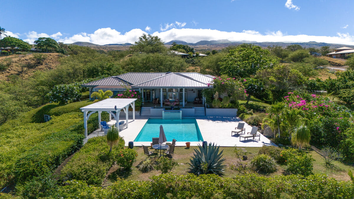 Home with a turquoise pool, white patio, and rolling hills beyond.