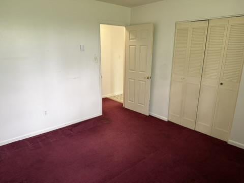 Empty bedroom with burgundy carpet and louvered closet doors.