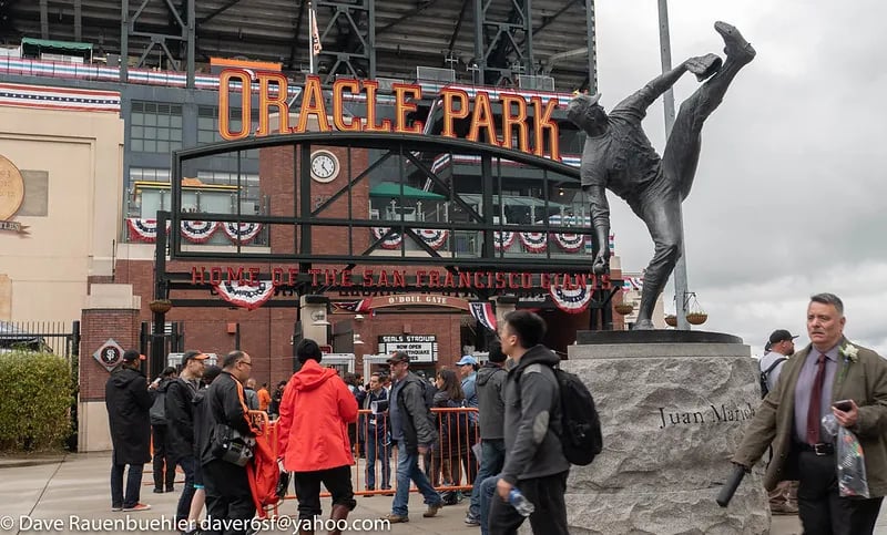 The Juan Marichal statue stands prominently in front of the Oracle Park O'Doul Gate entrance with fans gathering before a San Francisco Giants game.