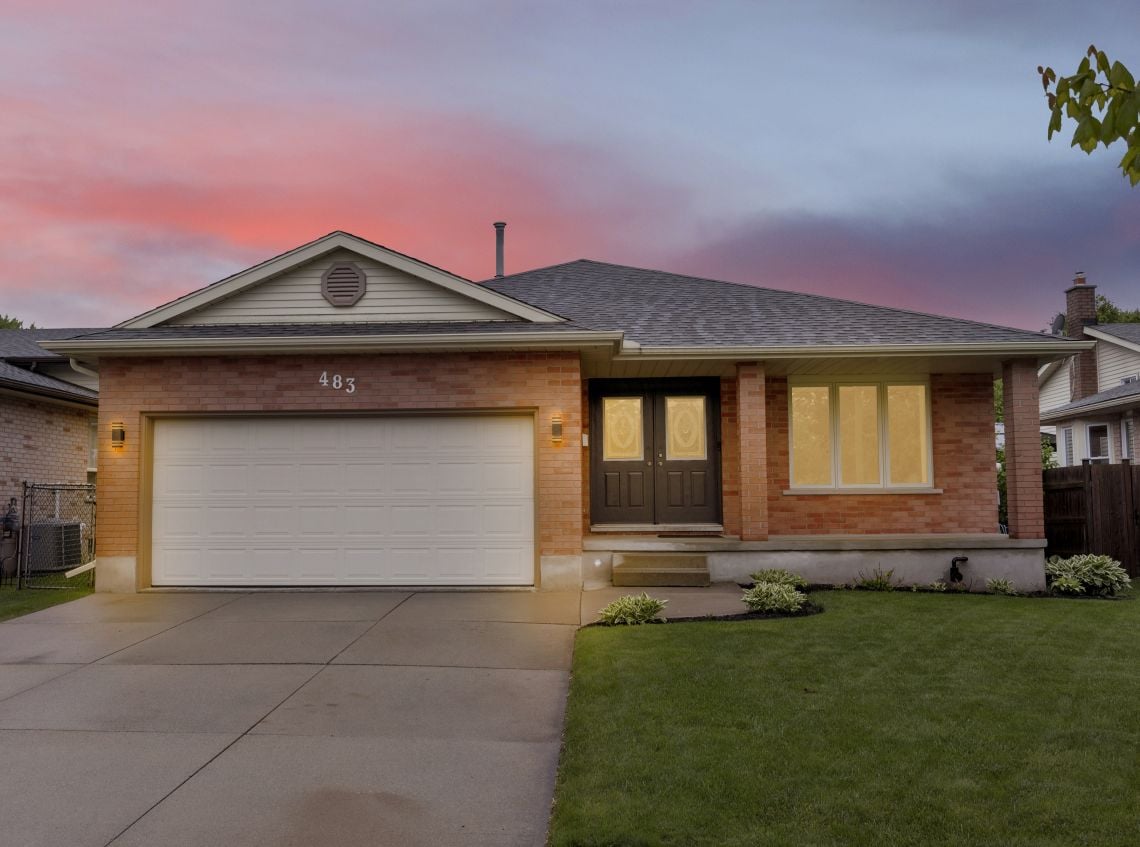 Single-story brick home with an attached double garage and warmly lit windows at dusk.