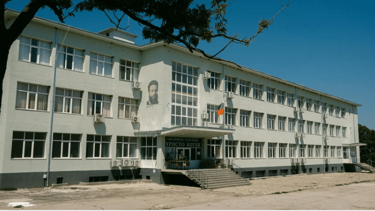 Long white building with rows of windows, a central stepped entrance, and a portrait painted on its facade.