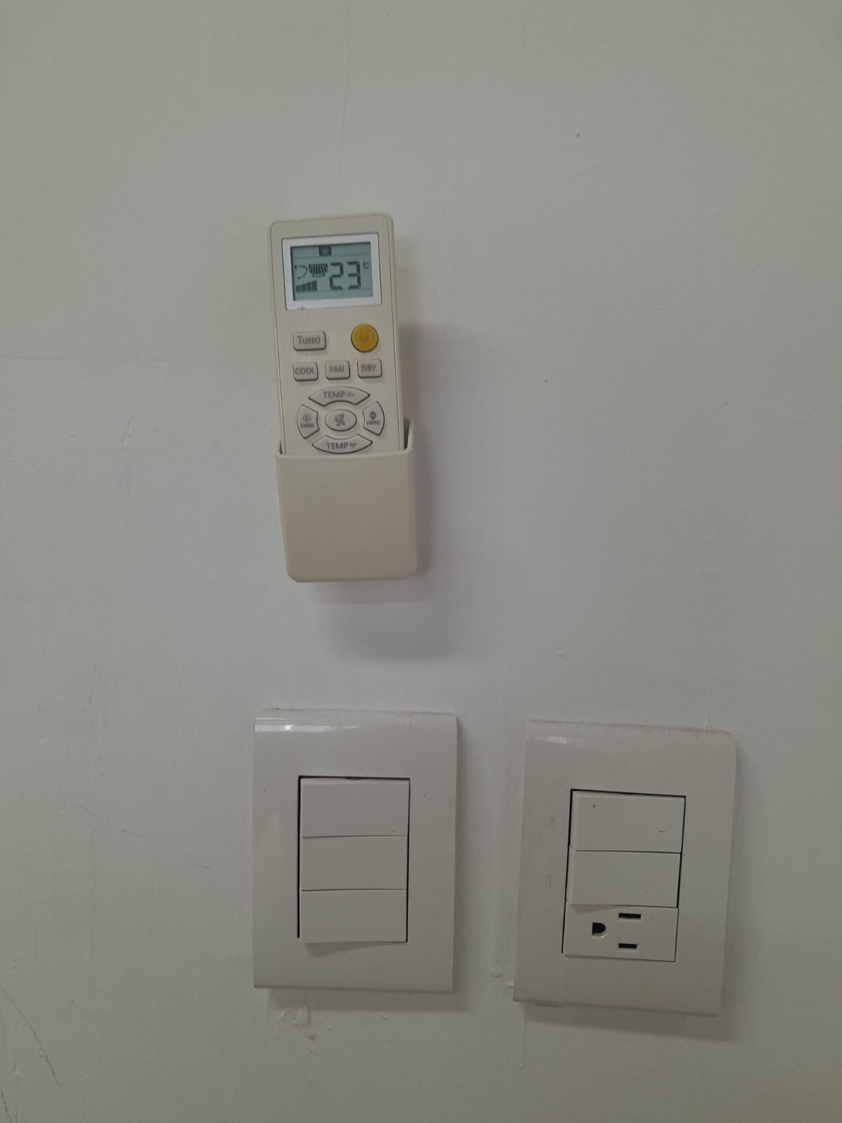 Air-conditioner remote mounted above two wall plates with switches and an electrical outlet.