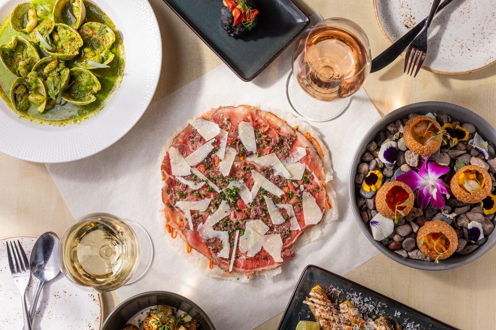 An overhead spread of Spanish tapas dishes at Vaca in Costa Mesa, including a burrata plate and wine.