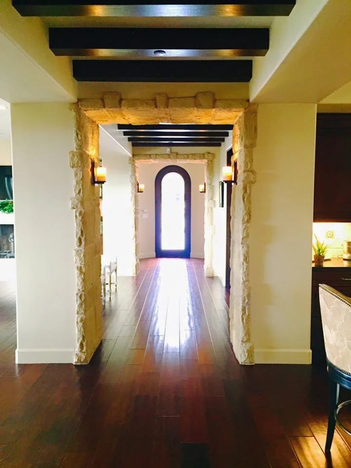 Hallway with stone archways, dark wood floors, ceiling beams, and an arched glass door.