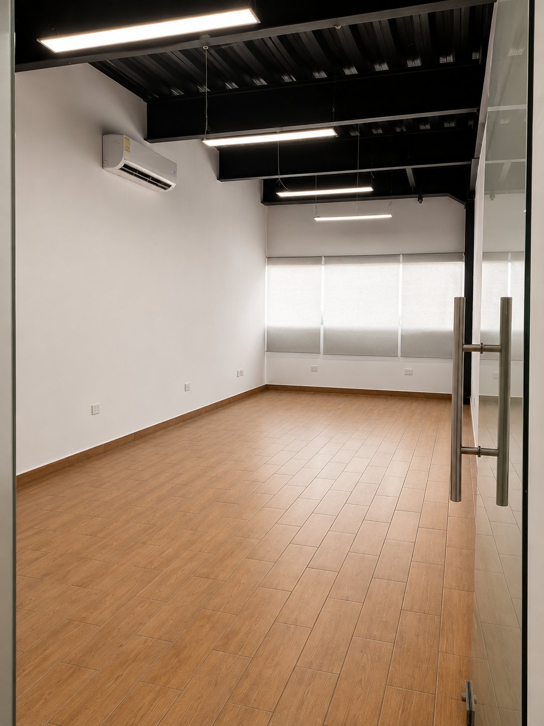 Vacant office suite with wood-look tile floors, exposed black ceiling, and shaded windows.