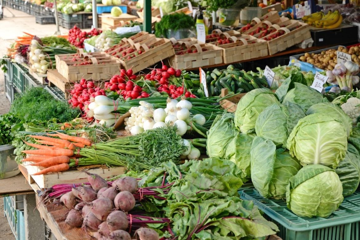 Fresh vegetables at an outdoor market, with cabbages, carrots, radishes, and beets in the foreground.