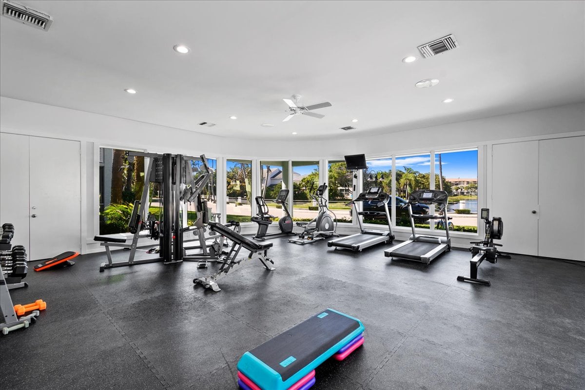 Condominium gym with cardio and weight equipment beside windows overlooking the water.