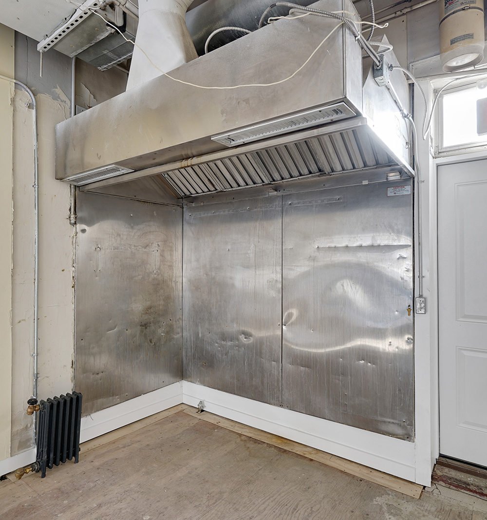 Commercial kitchen with a large stainless-steel exhaust hood and metal wall panels.