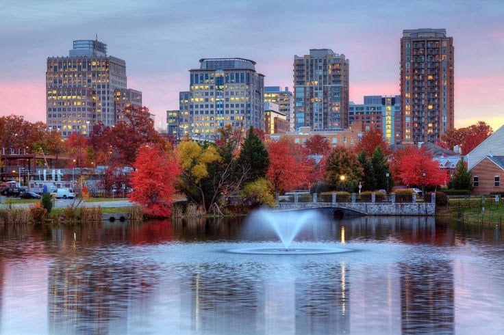 Reston skyline and autumn trees reflected in a lake, with a fountain in the foreground.