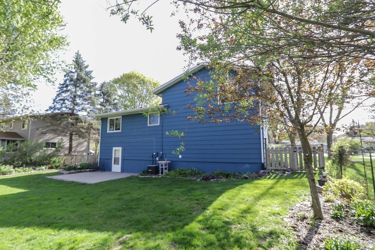 Blue house with a small patio and fenced, tree-lined lawn.