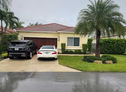 Single-story yellow home with a red tile roof, two cars, and palm trees.