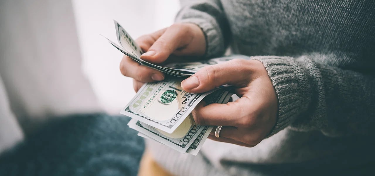 Hands count U.S. $100 bills.