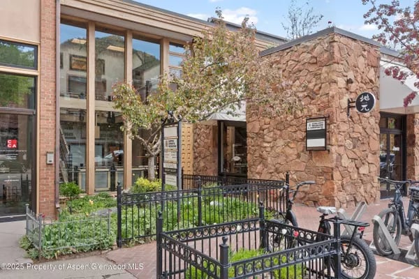 Stone-and-glass commercial building with a fenced garden and bicycles outside.