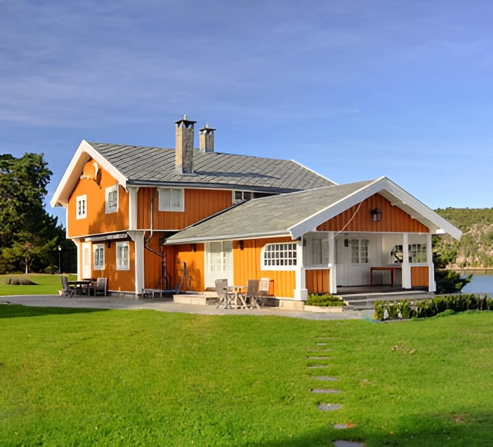 Orange-and-white vacation home with a covered patio, green lawn, and water nearby.