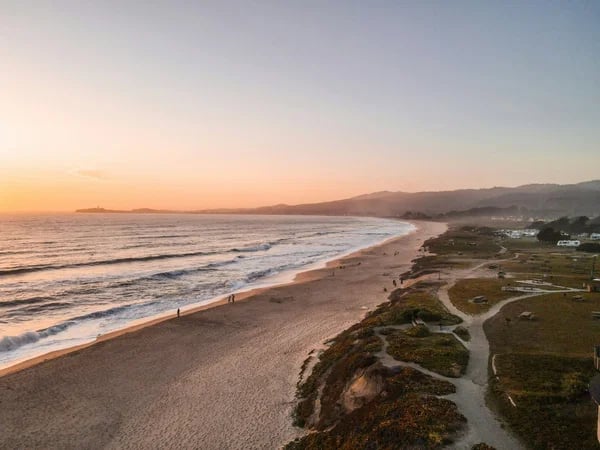 Half Moon Bay shoreline at sunset, with waves, sandy beach, coastal trails, and distant hills.