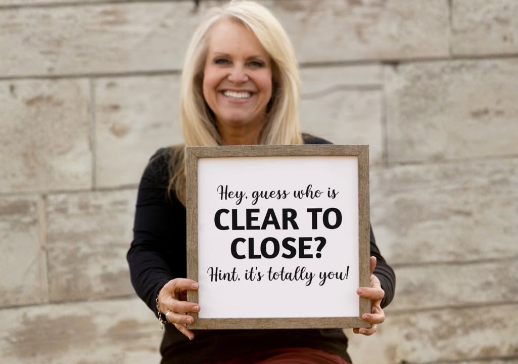 Sharla Ellis holding a sign that says "Hey, guess who is Clear to Close?" celebrating the exciting milestone before homebuyers receive the keys to their new home.