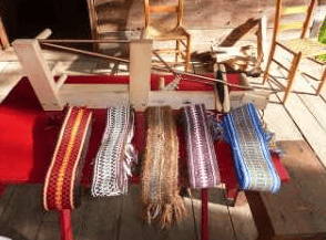 Colorful woven belts displayed on a wooden rack on a porch.