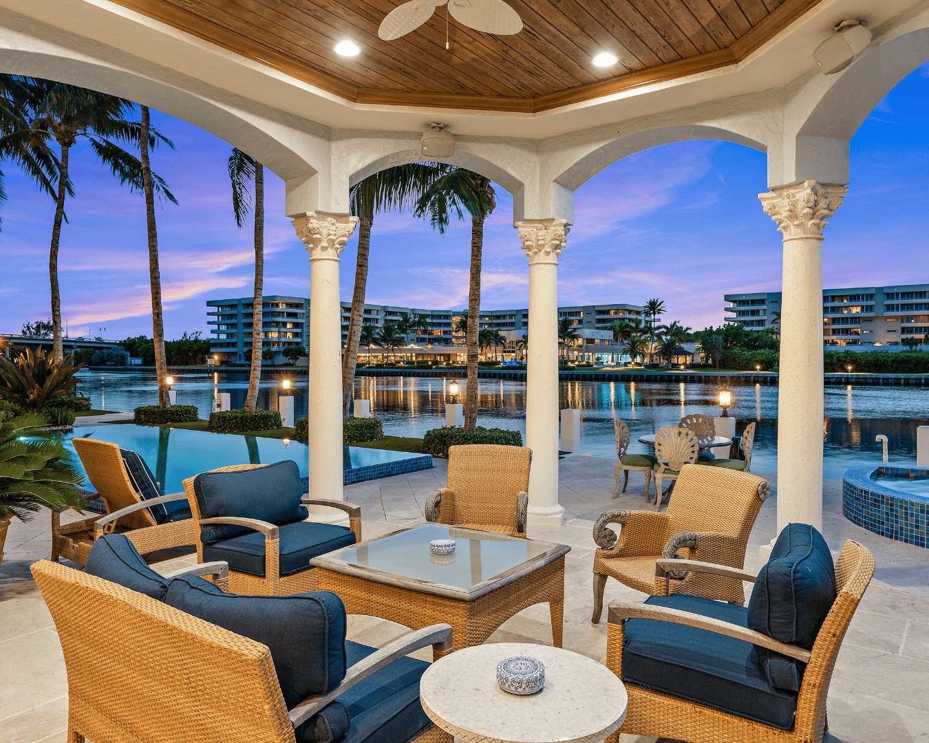 Covered loggia with Corinthian columns, arched openings, and a wood-plank ceiling overlooking the pool and Intracoastal Waterway at dusk in Delray Beach, Florida