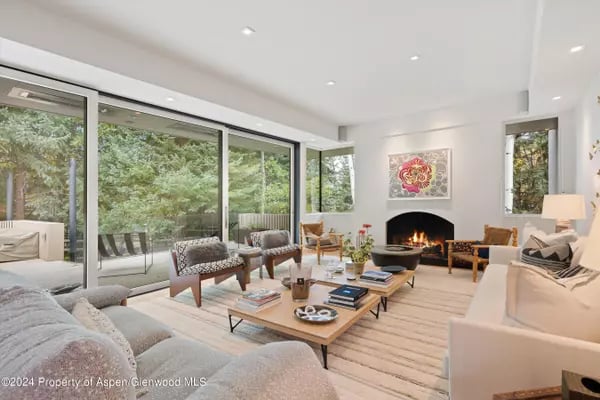 Living room with a central fireplace, contemporary furnishings, and glass doors overlooking trees.