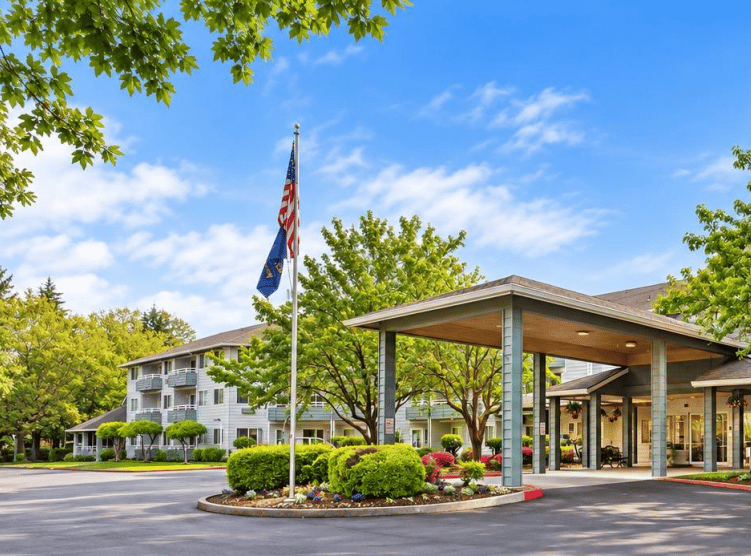 Senior living community exterior with a covered entrance, landscaped grounds, and flagpoles.