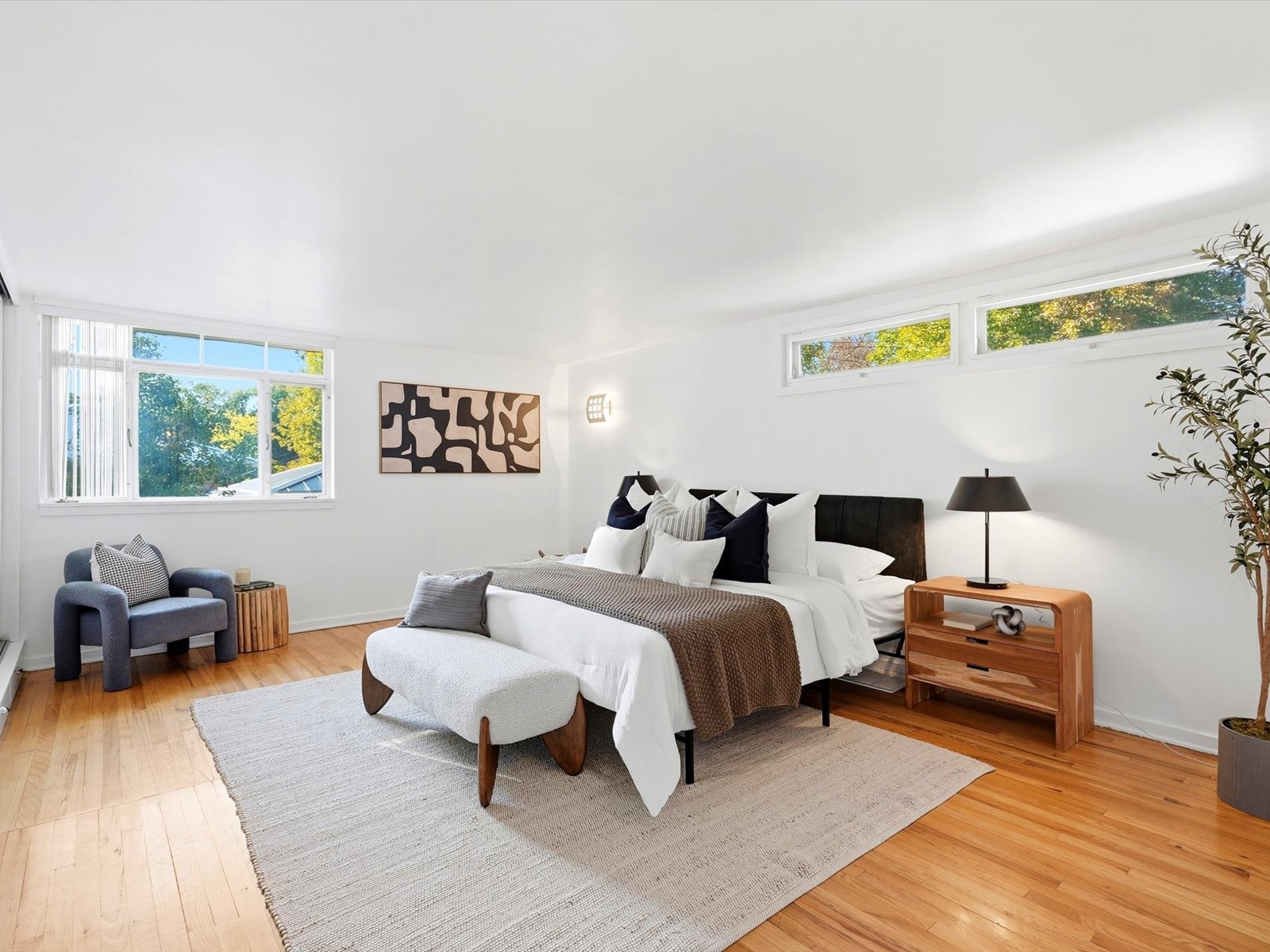 Staged bedroom with a white bed, blue armchair, hardwood floors, and high horizontal windows.
