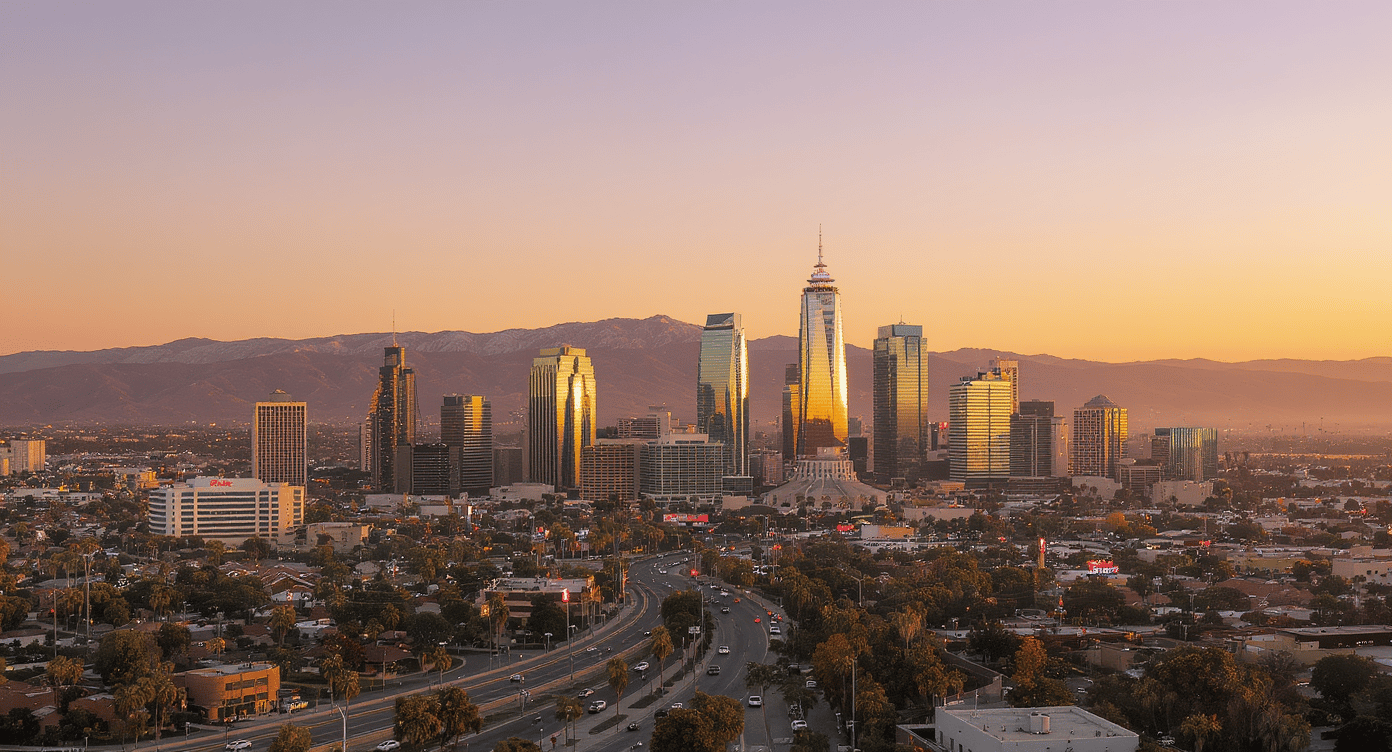 Downtown Los Angeles skyline glowing at sunset, with the San Gabriel Mountains behind it.