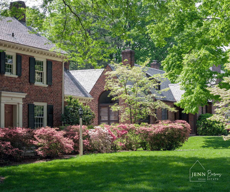 Red-brick homes with slate roofs, leafy trees, pink flowering shrubs, and a green lawn.