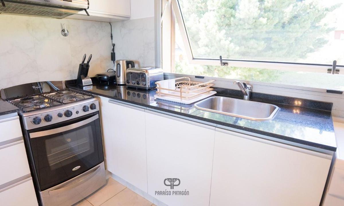 Apartment kitchen with a stainless-steel gas range, dark countertops, and a sink beneath a large window.
