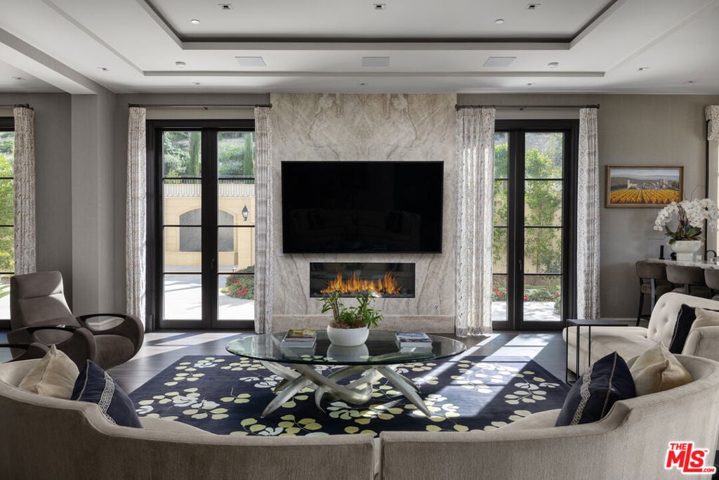 Living room with a marble fireplace wall, television, curved sofa, and tall windows.