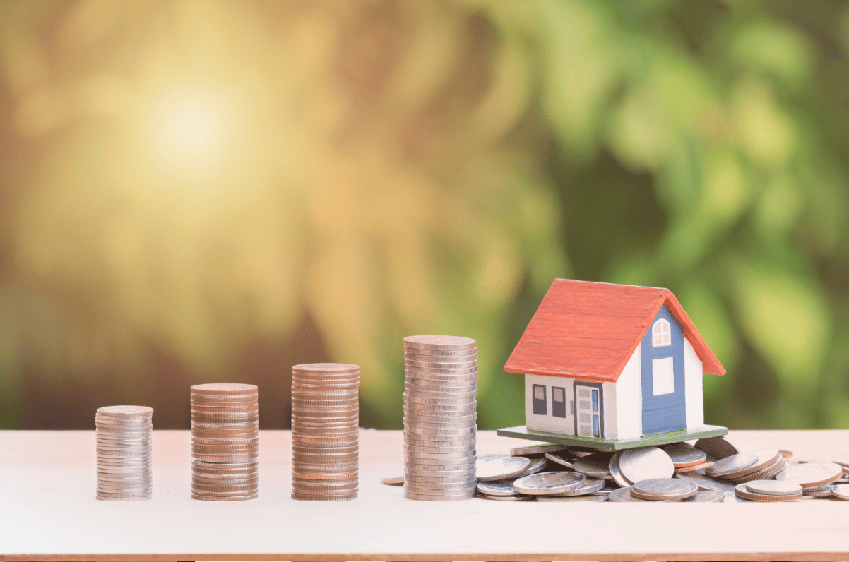 Miniature house on scattered coins beside four progressively taller coin stacks