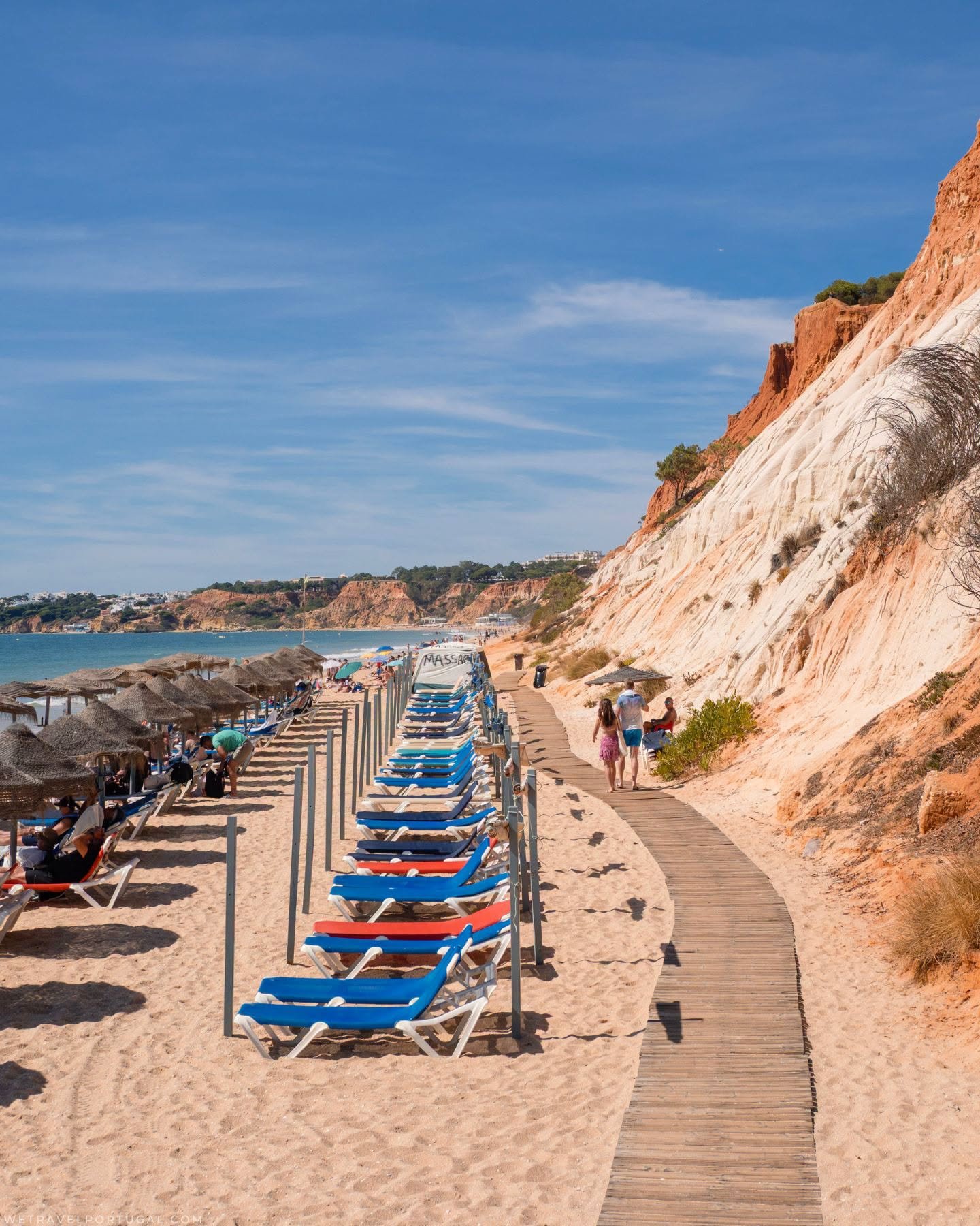 Rows of sun loungers and thatched parasols on the sand at Praia da Falesia, with a boardwalk running beneath red and white cliffs