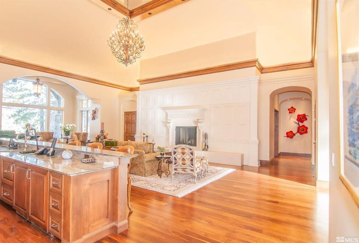 Open-plan kitchen and living room with a granite island, white fireplace, and tall arched windows.