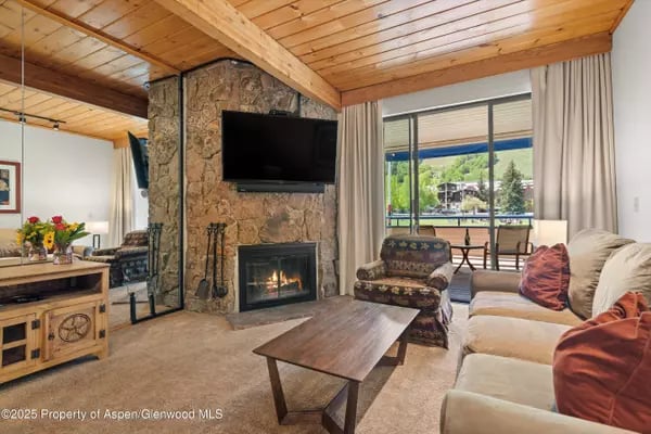 Living room with a stone fireplace, vaulted wood ceiling, and balcony overlooking mountains.