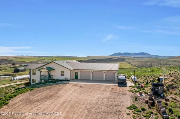 Rural home with three garage bays, a wide gravel driveway, and open countryside with distant mountains.