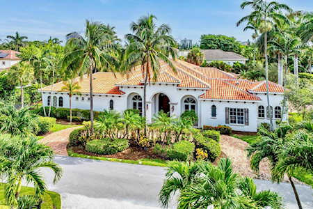 White stucco home with a red tile roof, arched entryway, and lush tropical landscaping.