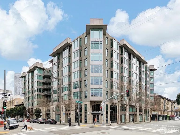 Modern multistory apartment building with glass windows and balconies on a city corner.