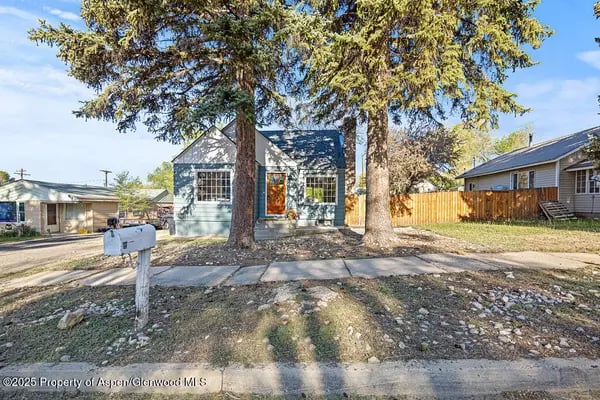 Pale blue house with an orange front door, framed by two large trees.