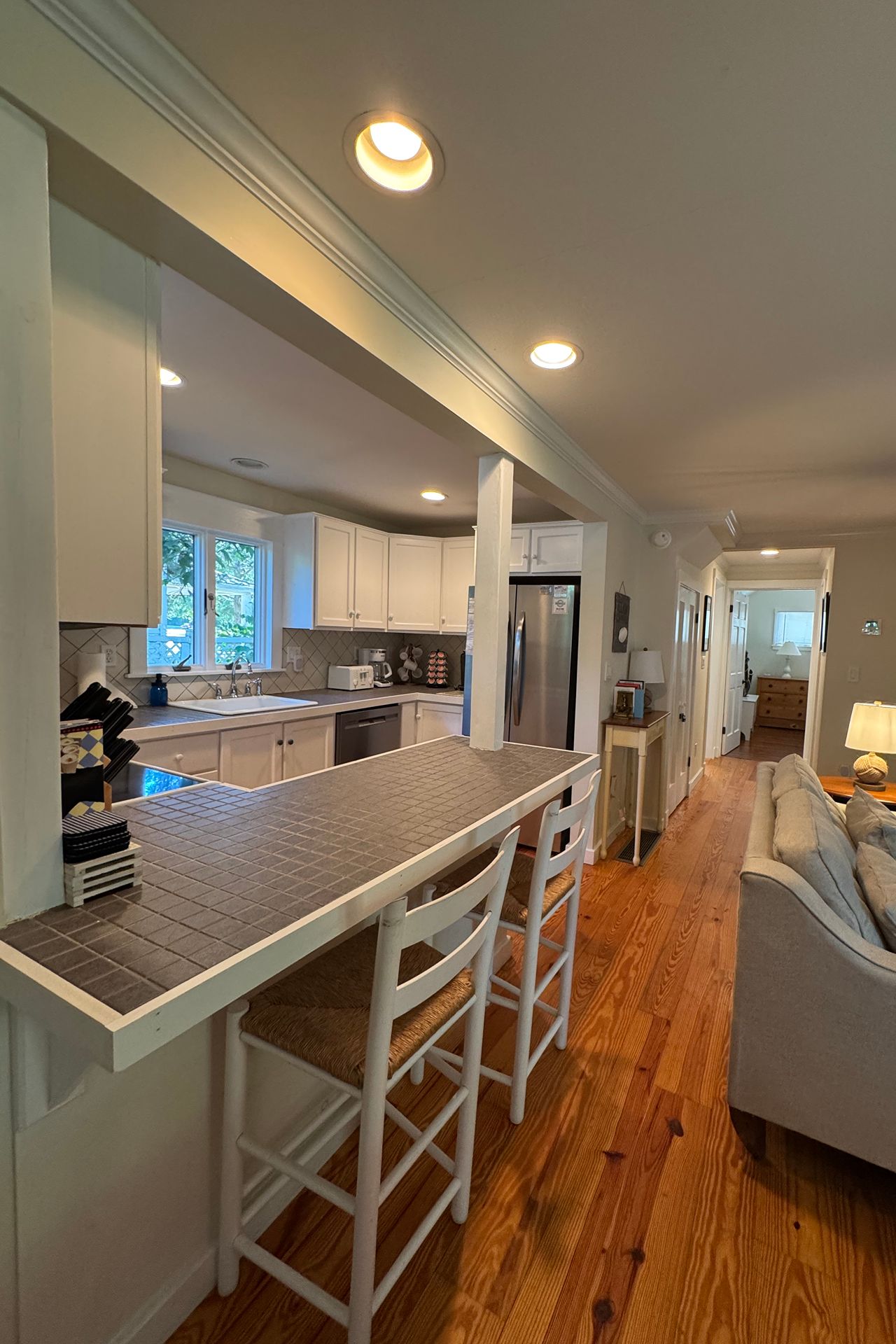 Kitchen with white cabinets, a tiled breakfast bar, stainless-steel refrigerator, and warm wood floors.